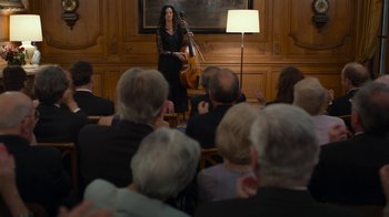 Movie still from “Happy End” (2017), directed by Michael Haneke – A woman is playing the cello in front of an audience; Wide shot, Over the shoulder angle