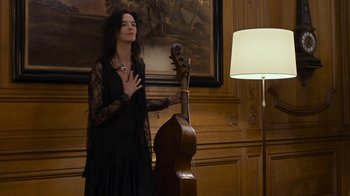 Movie still from “Happy End” (2017), directed by Michael Haneke – A woman in a black dress standing next to an upright bass; Medium shot, Low angle