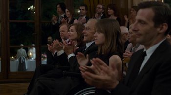 Movie still from “Happy End” (2017), directed by Michael Haneke – A group of people sitting in a room clapping at an event; Medium shot, Over the shoulder angle