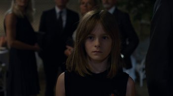 Movie still from “Happy End” (2017), directed by Michael Haneke – A young girl in a black dress is in front of a group of people; Close Up shot, Over the shoulder angle