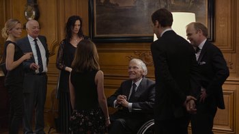 Movie still from “Happy End” (2017), directed by Michael Haneke – A man in a wheel chair talking to a group of people; Medium shot, High angle