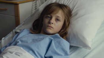 Movie still from “Happy End” (2017), directed by Michael Haneke – A young girl laying in a hospital bed with a blue blanket; Close Up shot, High angle
