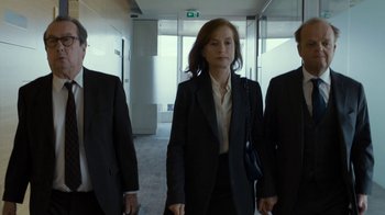 Movie still from “Happy End” (2017), directed by Michael Haneke – A woman in a black suit and a man in a black suit and a man in a black suit; Medium shot, Low angle