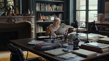 Movie still from “Happy End” (2017), directed by Michael Haneke – An older man sitting at a table reading a newspaper; Wide shot, High angle