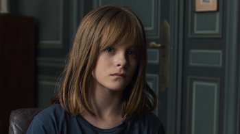 A young girl with long brown hair and bangs looking at the camera