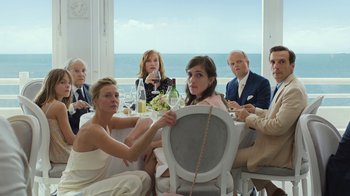 Movie still from “Happy End” (2017), directed by Michael Haneke – A group of people sitting at a table with ocean in the background; Medium shot, High angle