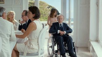 Movie still from “Happy End” (2017), directed by Michael Haneke – An older man in a wheelchair at a table with people; Medium shot, Over the shoulder angle