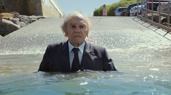 Movie still from “Happy End” (2017), directed by Michael Haneke – An old man in a suit and tie in a body of water; Wide shot, High angle