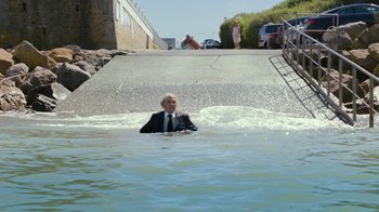 Movie still from “Happy End” (2017), directed by Michael Haneke – A man in a suit and tie in the middle of a street; Wide shot, High angle