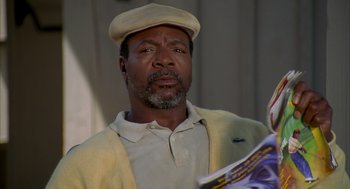 Movie still from “Happy Gilmore” (1996), directed by Dennis Dugan – An older man wearing a hat and holding a magazine; Close Up shot, Low angle