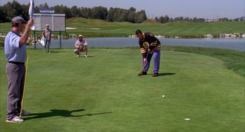 Movie still from “Happy Gilmore” (1996), directed by Dennis Dugan – Two men are playing a game of golf on a green; Extreme Wide shot, High angle