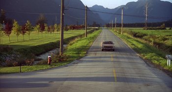 Movie still from “Happy Gilmore” (1996), directed by Dennis Dugan – A car driving down a road near a grassy field; Extreme Wide shot, High angle