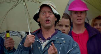 Movie still from “Happy Gilmore” (1996), directed by Dennis Dugan – A man in a rain coat and a hat holding an umbrella; Close Up shot, Low angle