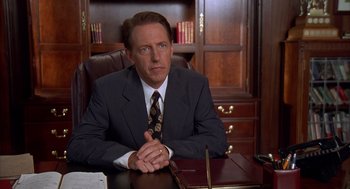 Movie still from “Happy Gilmore” (1996), directed by Dennis Dugan – A man sitting at a desk wearing a suit and tie; Close Up shot, High angle