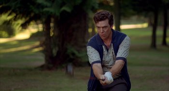Movie still from “Happy Gilmore” (1996), directed by Dennis Dugan – A man swinging a baseball bat on a field; Medium shot, Over the shoulder angle