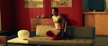 Movie still from “Hard Candy” (2005), directed by David Slade – A woman sitting on top of a couch in front of a red wall; Medium shot, High angle