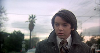 Movie still from “Harold and Maude” (1971), directed by Hal Ashby – A man in a coat and tie standing in front of a palm tree; Close Up shot, Low angle