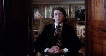 Movie still from “Harold and Maude” (1971), directed by Hal Ashby – A man in a suit and tie sitting in front of a painting; Medium shot, Low angle