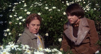 Movie still from “Harold and Maude” (1971), directed by Hal Ashby – A woman and a young boy sitting in a field of flowers; Medium shot, High angle