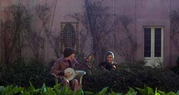 Movie still from “Harold and Maude” (1971), directed by Hal Ashby – A man and a woman sitting on a chair playing music; Wide shot, High angle