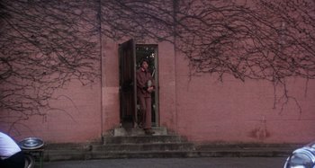 Movie still from “Harold and Maude” (1971), directed by Hal Ashby – A man standing in front of a pink building; Wide shot, Low angle