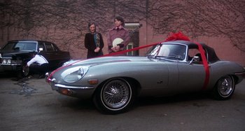 Movie still from “Harold and Maude” (1971), directed by Hal Ashby – Two women standing in front of a car with a red bow on it; Wide shot, High angle
