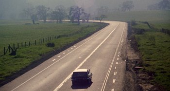 Movie still from “Harold and Maude” (1971), directed by Hal Ashby – A car driving down a road near some trees; Extreme Wide shot, High angle