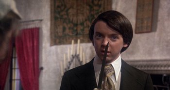 Movie still from “Harold and Maude” (1971), directed by Hal Ashby – A man in a suit holding a knife in his mouth; Close Up shot, Over the shoulder angle