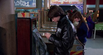 Movie still from “Harold and Maude” (1971), directed by Hal Ashby – A young man in a leather jacket looking at an arcade machine; Medium shot, High angle