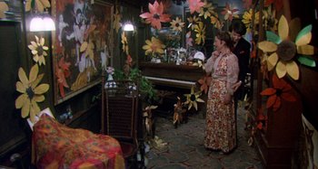Movie still from “Harold and Maude” (1971), directed by Hal Ashby – A woman standing in front of a piano in a living room; Wide shot, High angle