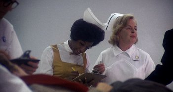 Movie still from “Harold and Maude” (1971), directed by Hal Ashby – A woman in a nurse's uniform writing on a clipboard next to another woman; Medium shot, Low angle
