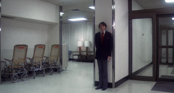 Movie still from “Harold and Maude” (1971), directed by Hal Ashby – A man in a suit and tie standing in a room; Wide shot, Low angle