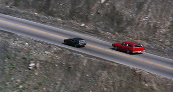 Movie still from “Harold and Maude” (1971), directed by Hal Ashby – A red car and a black car on the side of the road; Extreme Wide shot, High angle