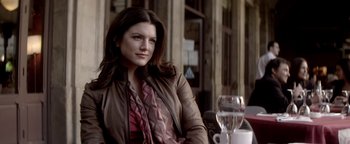 Movie still from “Haywire” (2011), directed by Steven Soderbergh – A woman sitting at an outdoor table with a glass of water; Close Up shot, Over the shoulder angle