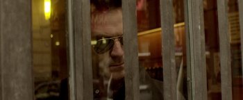 Movie still from “Haywire” (2011), directed by Steven Soderbergh – A man wearing sunglasses looking through a fence; Extreme Close Up shot, Low angle