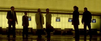 Movie still from “Haywire” (2011), directed by Steven Soderbergh – Two men are standing in an airport waiting area; Wide shot, Low angle