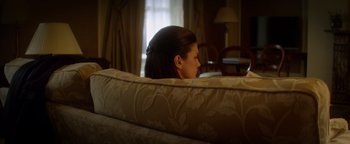 Movie still from “Haywire” (2011), directed by Steven Soderbergh – A woman sitting on top of a couch in a living room; Medium shot, Over the shoulder angle