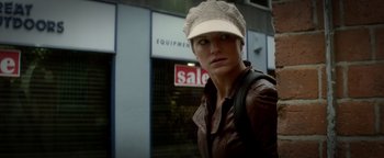 Movie still from “Haywire” (2011), directed by Steven Soderbergh – A woman wearing a hat standing in front of a building; Close Up shot, Low angle