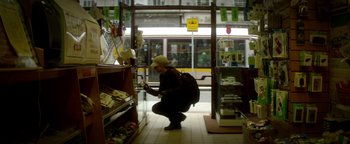 Movie still from “Haywire” (2011), directed by Steven Soderbergh – A person with a backpack is looking at something in a store; Wide shot, High angle
