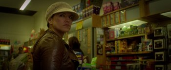 Movie still from “Haywire” (2011), directed by Steven Soderbergh – A woman wearing a hat standing in front of shelves of books; Close Up shot, Low angle