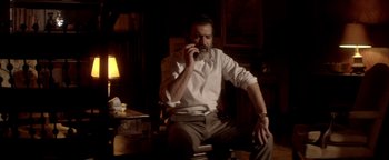 Movie still from “Haywire” (2011), directed by Steven Soderbergh – A man sitting at a table drinking a beverage; Medium shot, Low angle