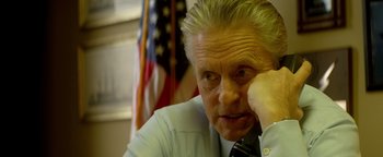 Movie still from “Haywire” (2011), directed by Steven Soderbergh – An older man sitting in front of an american flag; Close Up shot, High angle