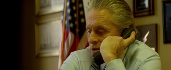 Movie still from “Haywire” (2011), directed by Steven Soderbergh – An older man talking on a phone in front of an american flag; Close Up shot, High angle