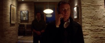 Movie still from “Haywire” (2011), directed by Steven Soderbergh – A man talking on a cell phone while another man watches; Medium shot, Low angle