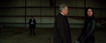Movie still from “Haywire” (2011), directed by Steven Soderbergh – A man in a suit and tie standing in an empty warehouse; Wide shot, Over the shoulder angle