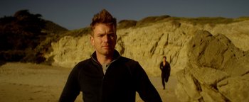Movie still from “Haywire” (2011), directed by Steven Soderbergh – A man standing on a sandy beach next to a woman; Close Up shot, Over the shoulder angle