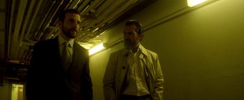 Movie still from “Haywire” (2011), directed by Steven Soderbergh – A man with a long beard standing next to another man in a suit; Medium shot, Low angle