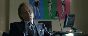 Movie still from “Headhunters” (2011), directed by Morten Tyldum – A man sitting in front of a wall of pictures; Medium shot, Over the shoulder angle