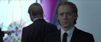 Movie still from “Headhunters” (2011), directed by Morten Tyldum – A man wearing a suit and tie standing next to another man; Close Up shot, Over the shoulder angle