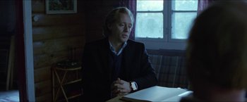 Movie still from “Headhunters” (2011), directed by Morten Tyldum – A man sitting at a table in front of a window; Medium shot, Low angle